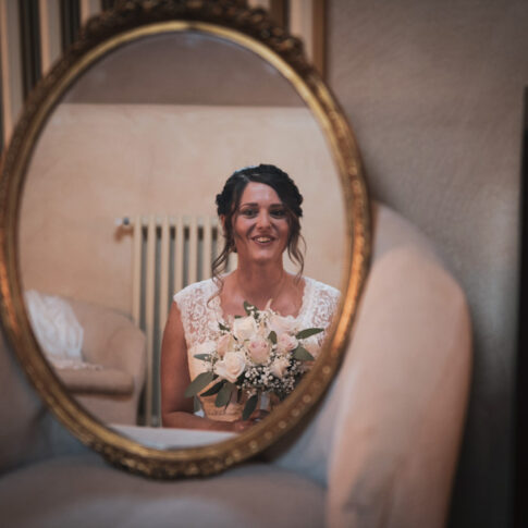 riflesso nello specchio della sposa sorridente col mazzolino in mano, in attesa di scendere per la cerimonia all'agriturismo di Colleoli